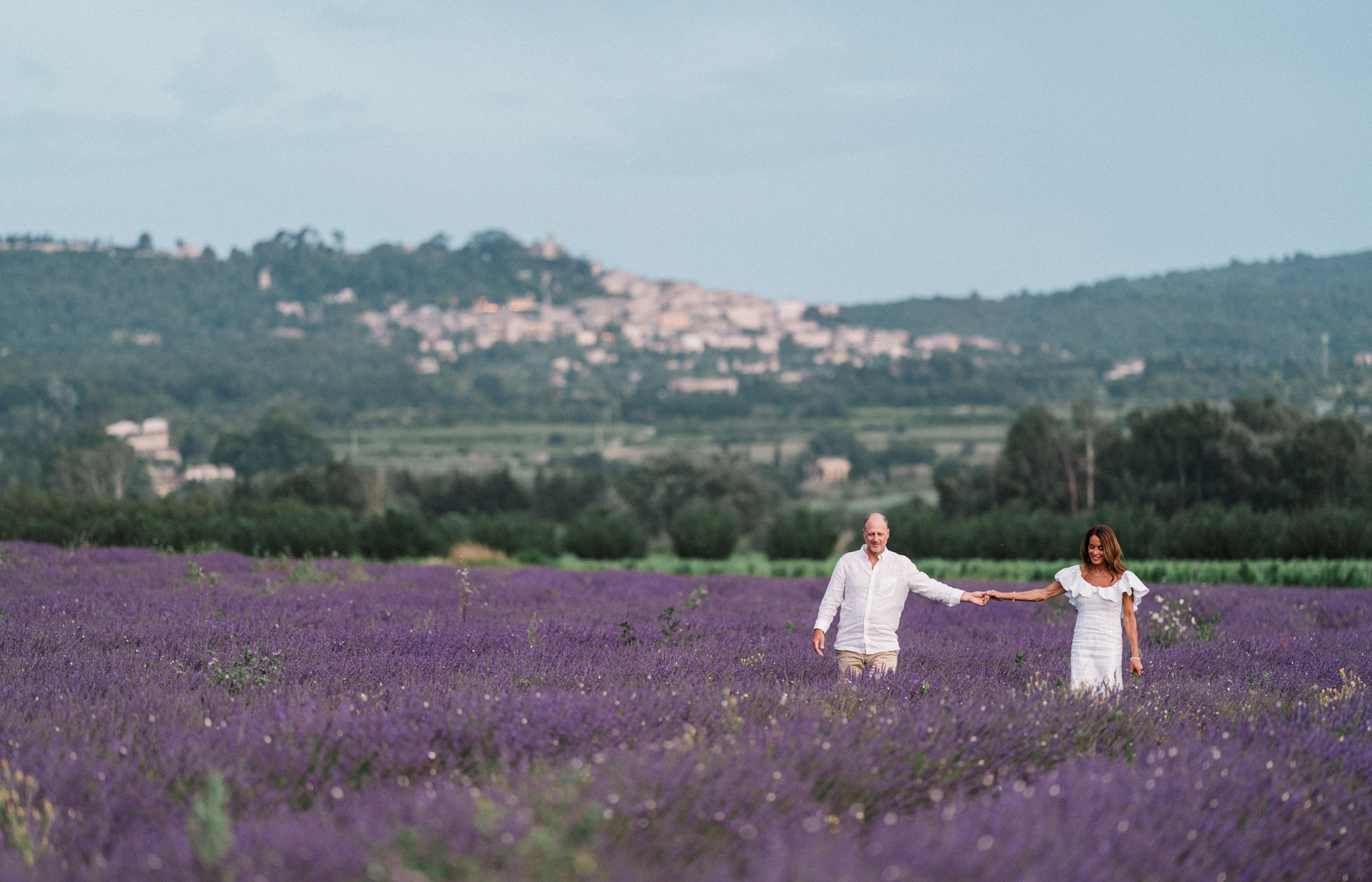 couple walking in lavender field with village in the background