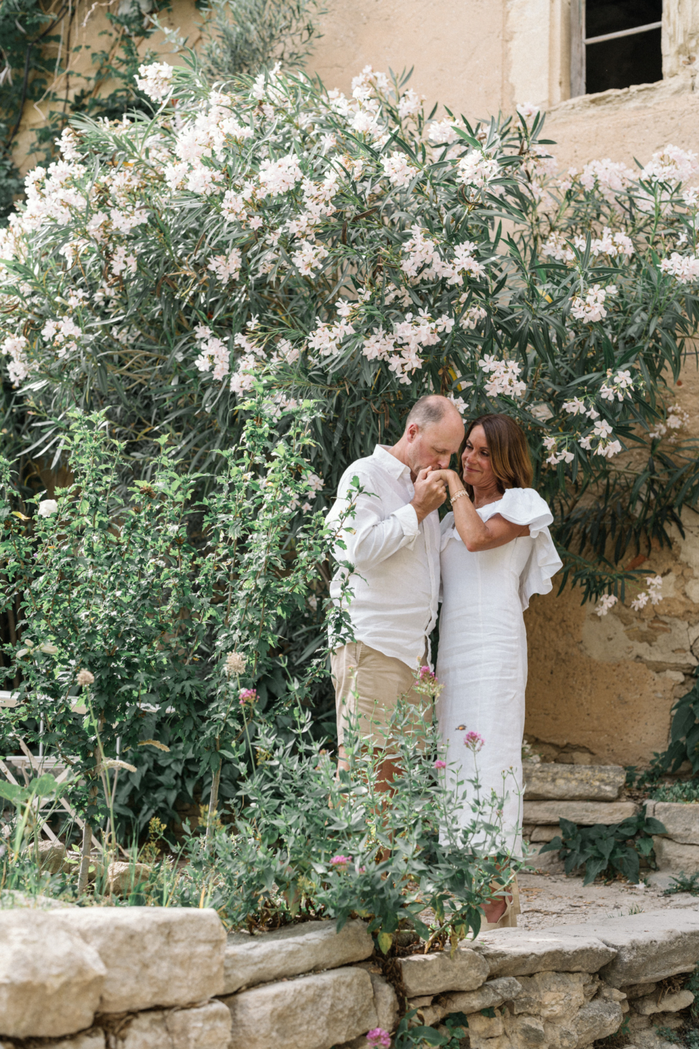 husband kisses wife's hand with white flowers in background