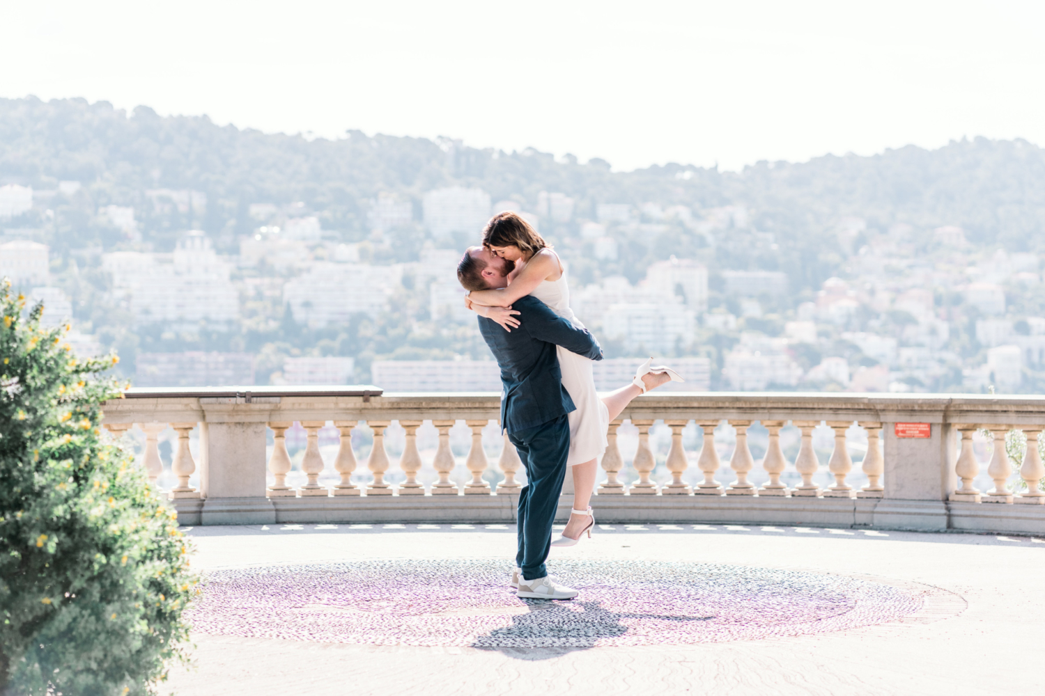 man kisses and lifts woman in air with beautiful view in nice france