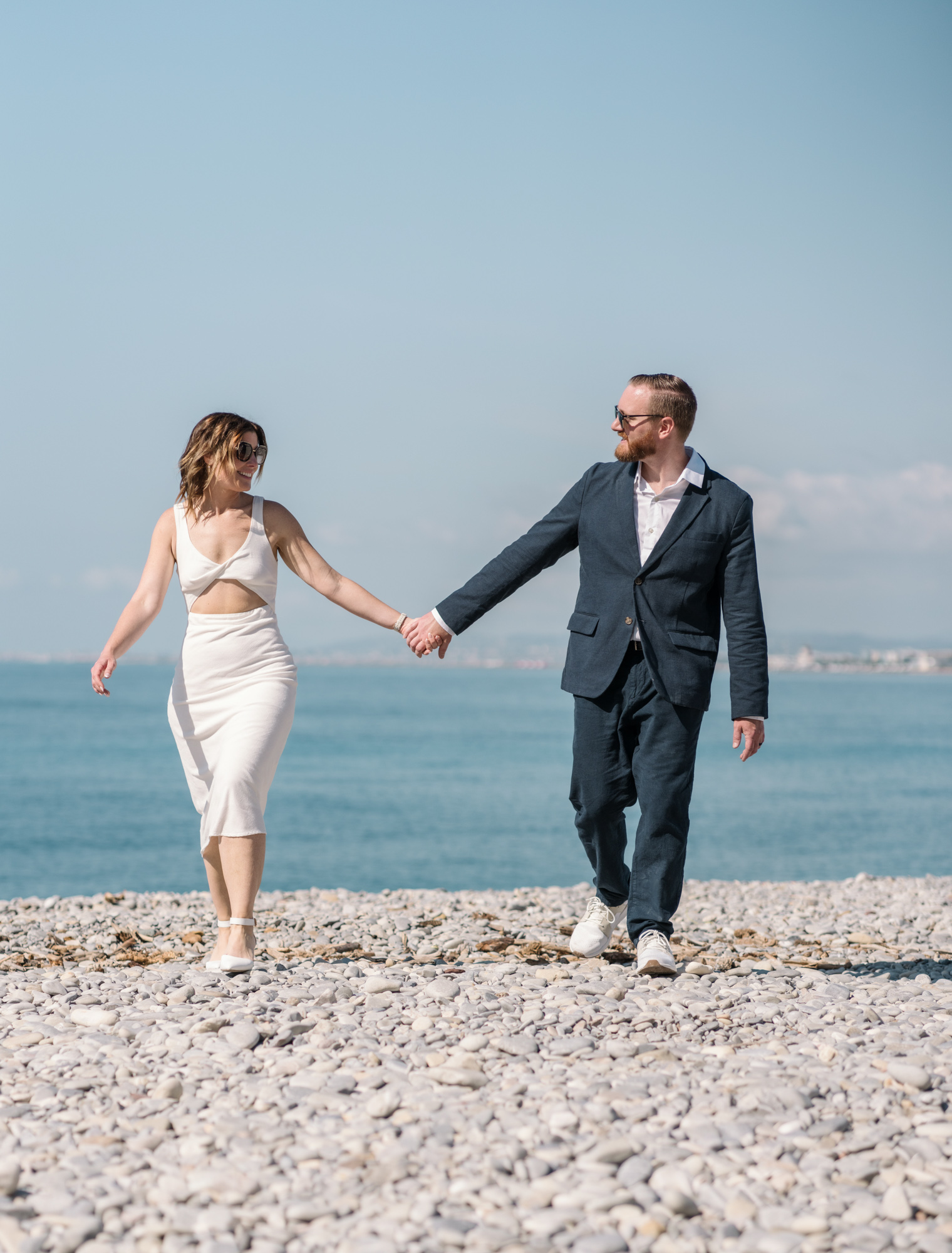 happy couple laugh and walk on stone beach in nice france