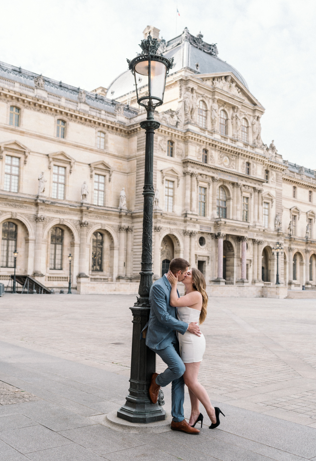 engaged couple kiss next to lamp post at louvre in paris