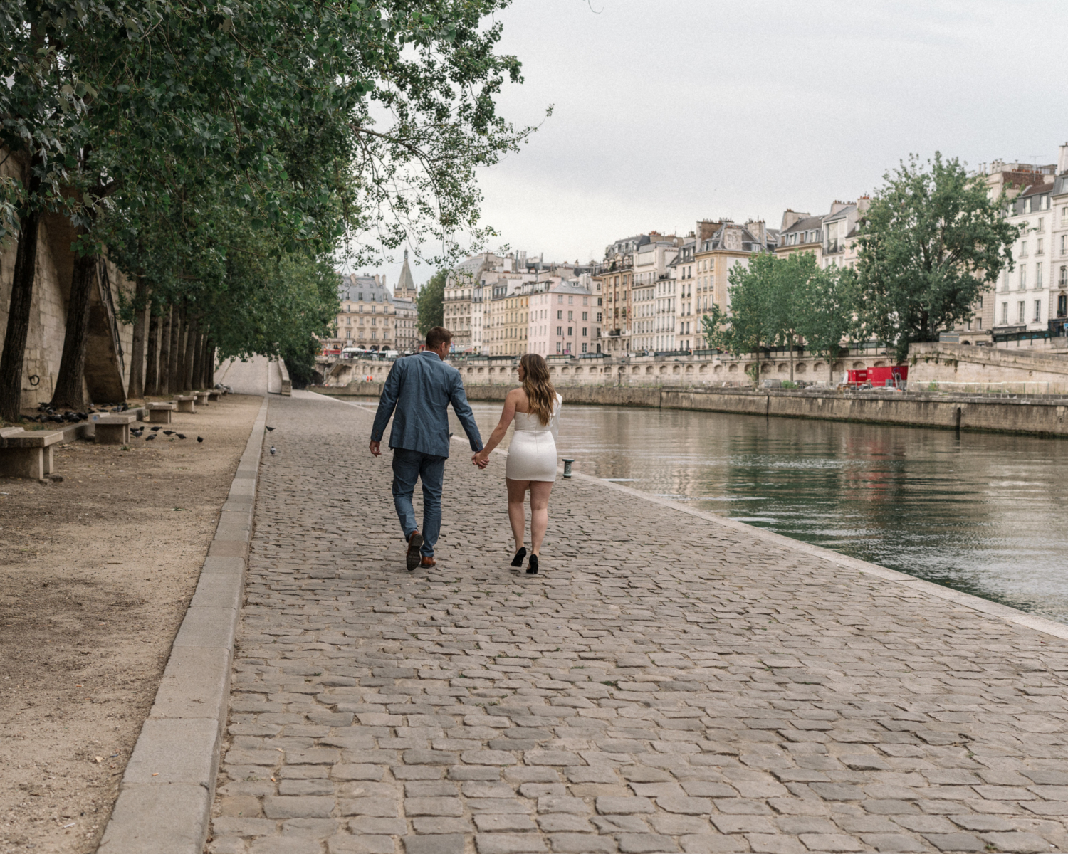 engaged couple walk hand in hand along the seine river in paris