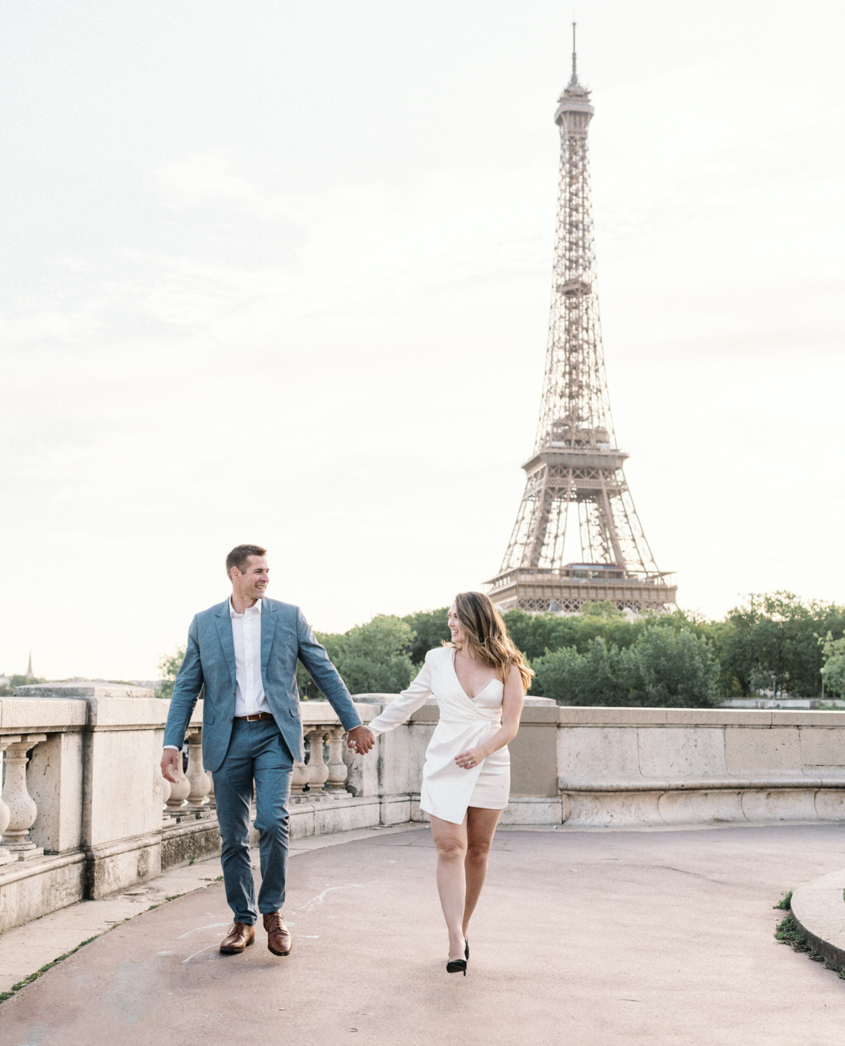 engaged couple smile and walk hand in hand with view of eiffel tower