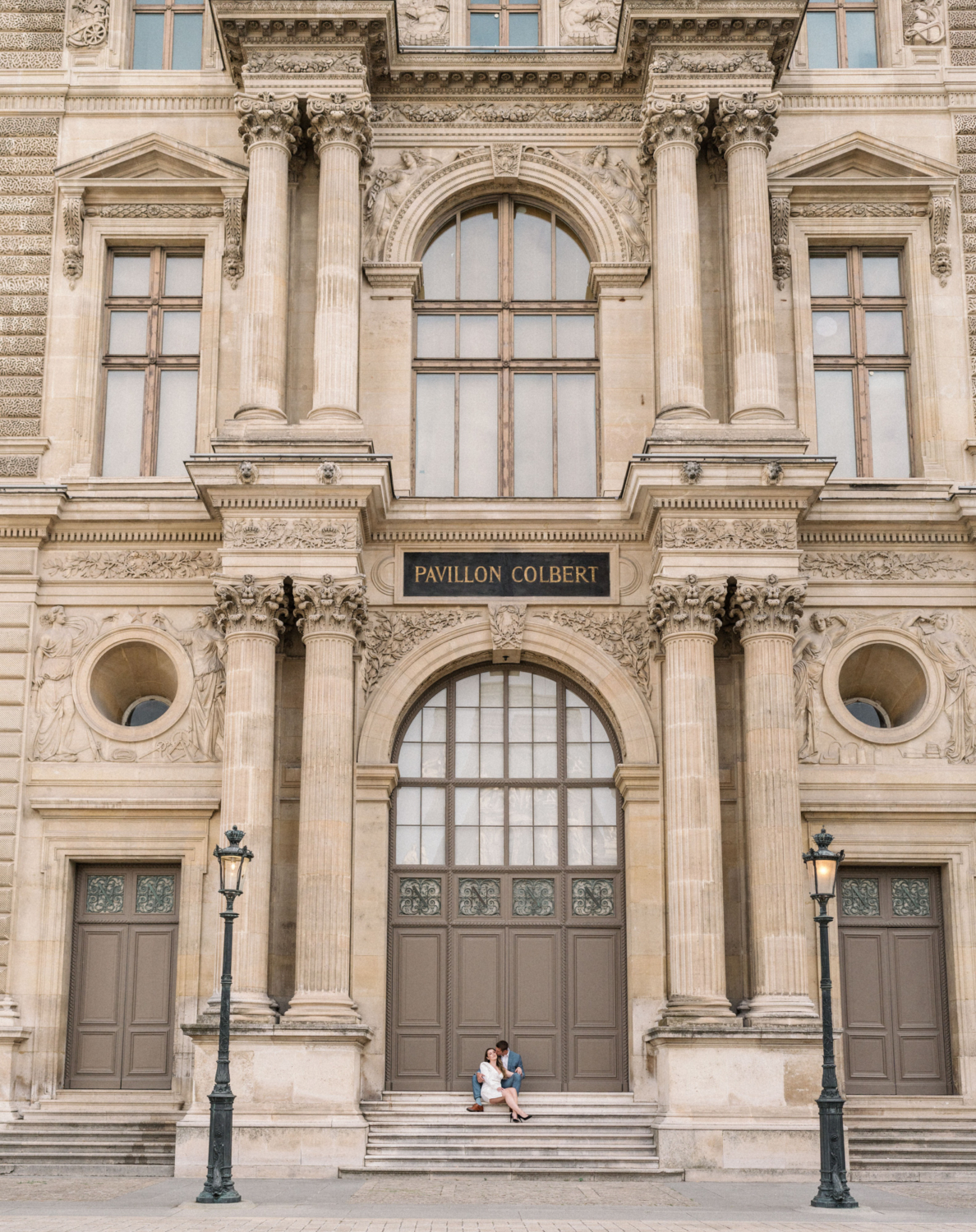 engaged couple sit on staircase at louvre museum in paris