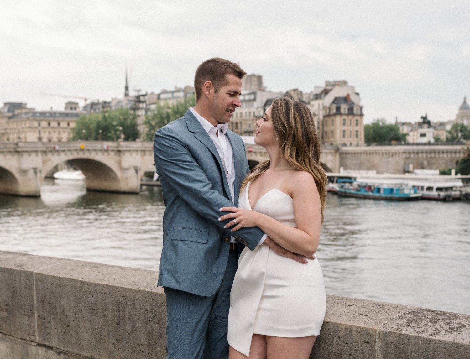 engaged couple hold each other along the river side in paris