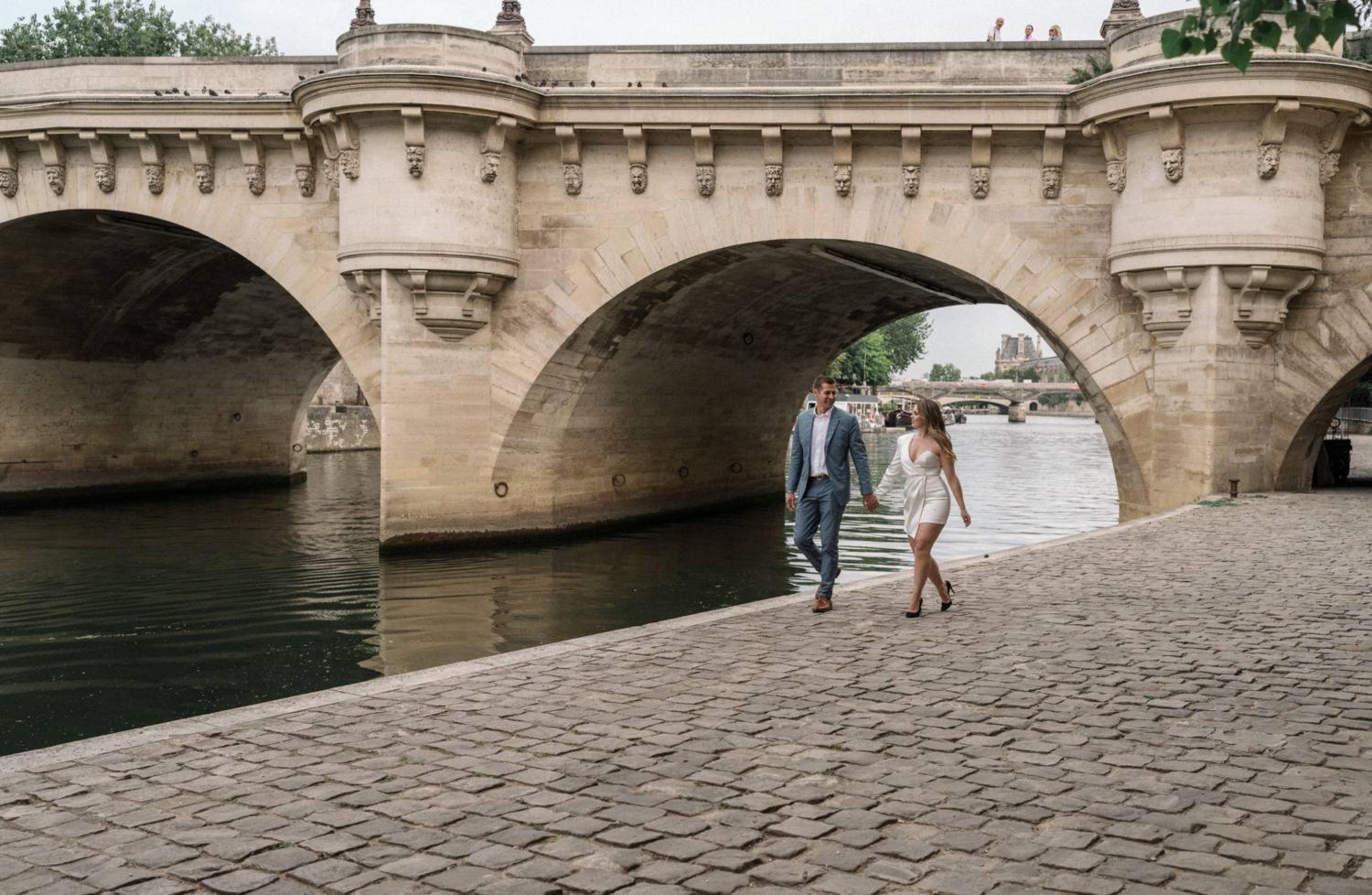 engaged couple walk hand in hand along seine river in paris