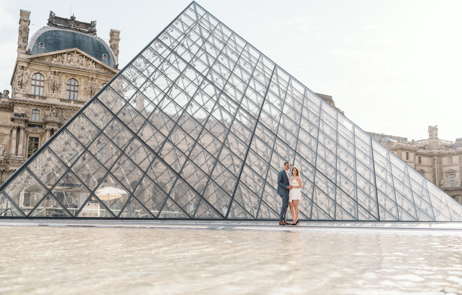 engaged couple pose at glass pyramid at louvre in paris