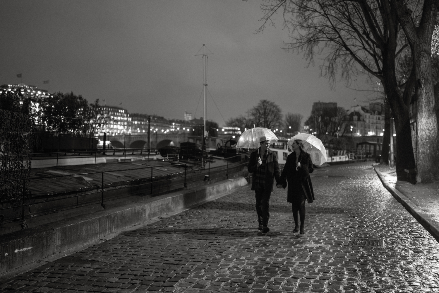 engaged couple with umbrellas walk at night in paris