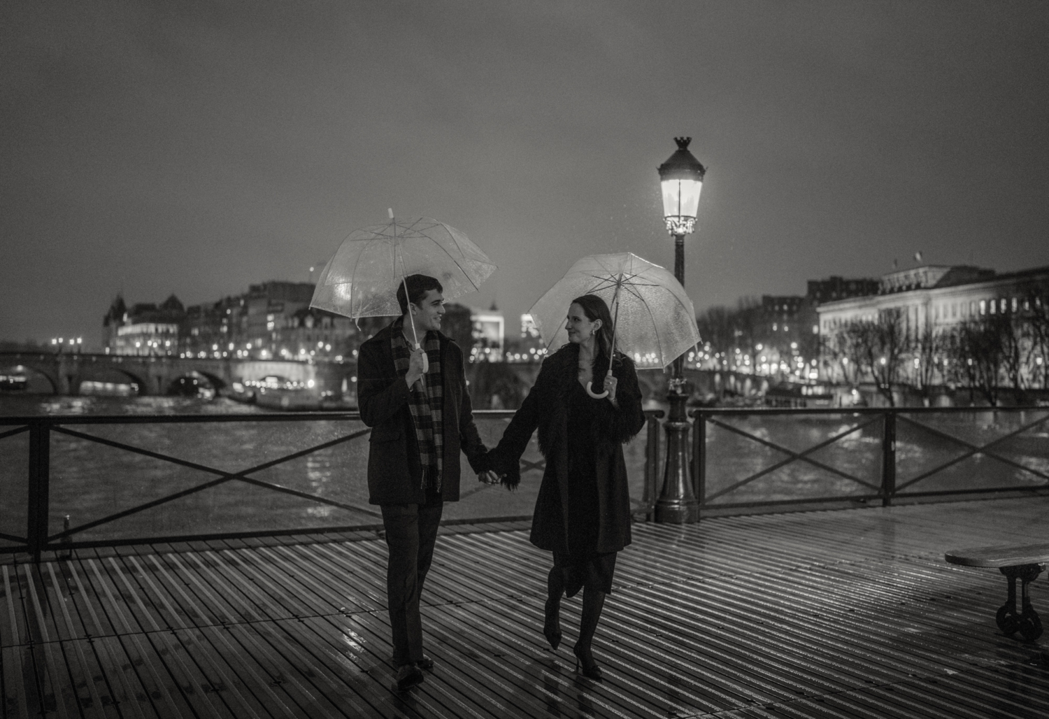 engaged couple with umbrellas walk on pont des arts at night