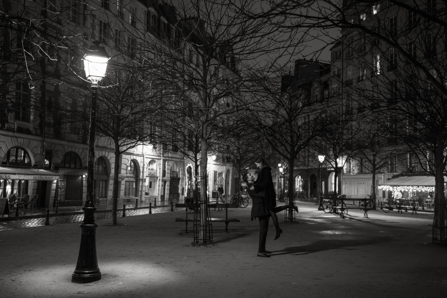 man lifts woman in air at place dauphine at night in paris