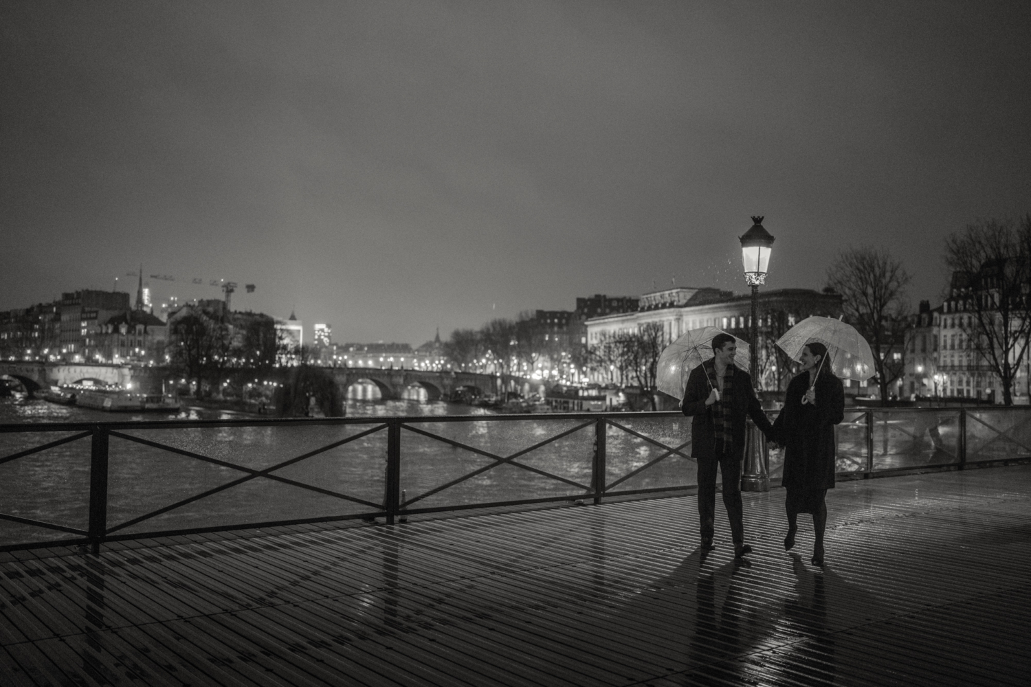 engaged couple with umbrellas walk on pont des arts in the rain in paris