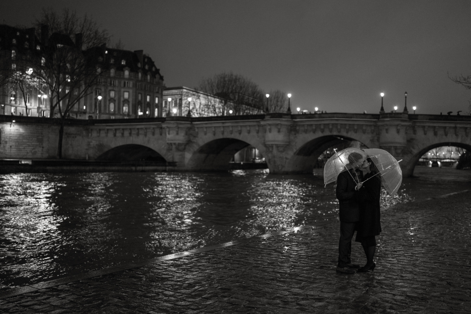 engaged couple with umbrellas kiss near pont neuf in paris