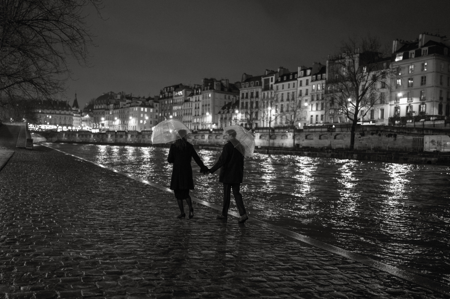 engaged couple with umbrellas walk in paris at night