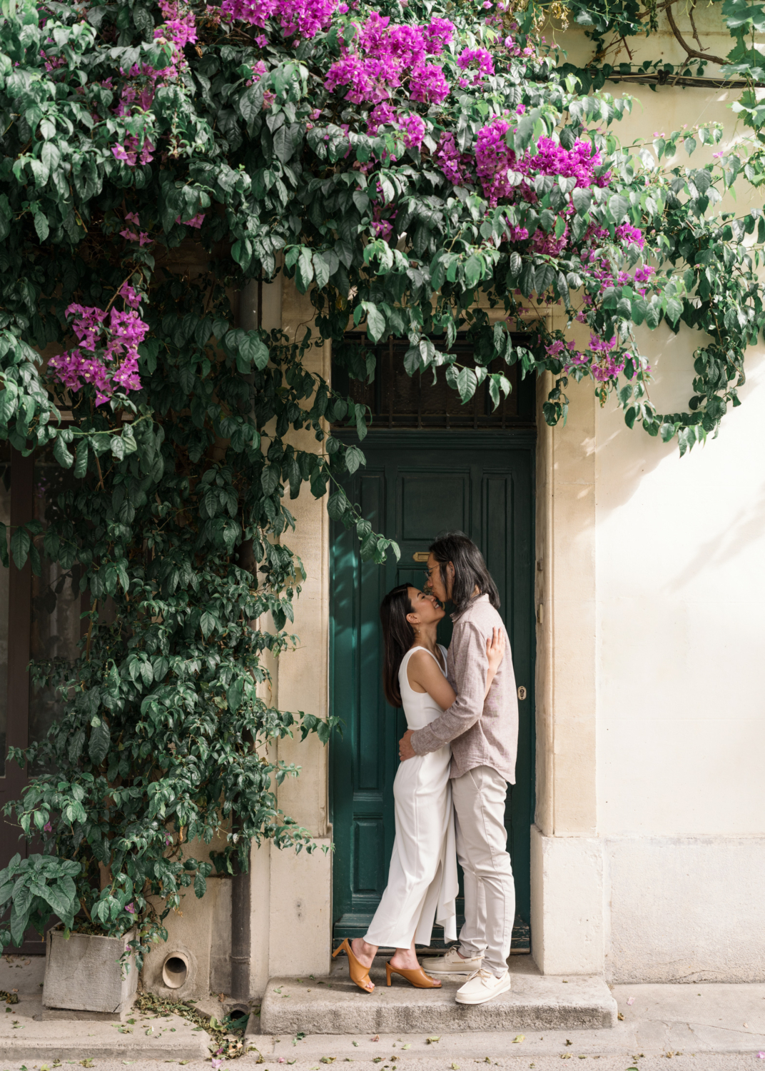 chinese couple embrace in front of green door surround by purple bougainvillea