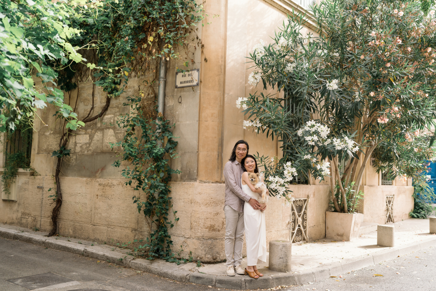 chinese couple hold Pomeranian dog and pose near white flowers in arles france