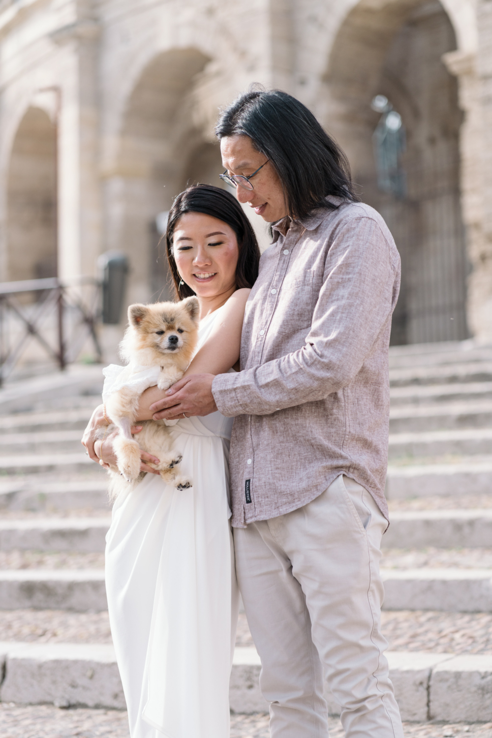 chinese couple hold their Pomeranian dog on the steps of the roman amphitheatre in arles france