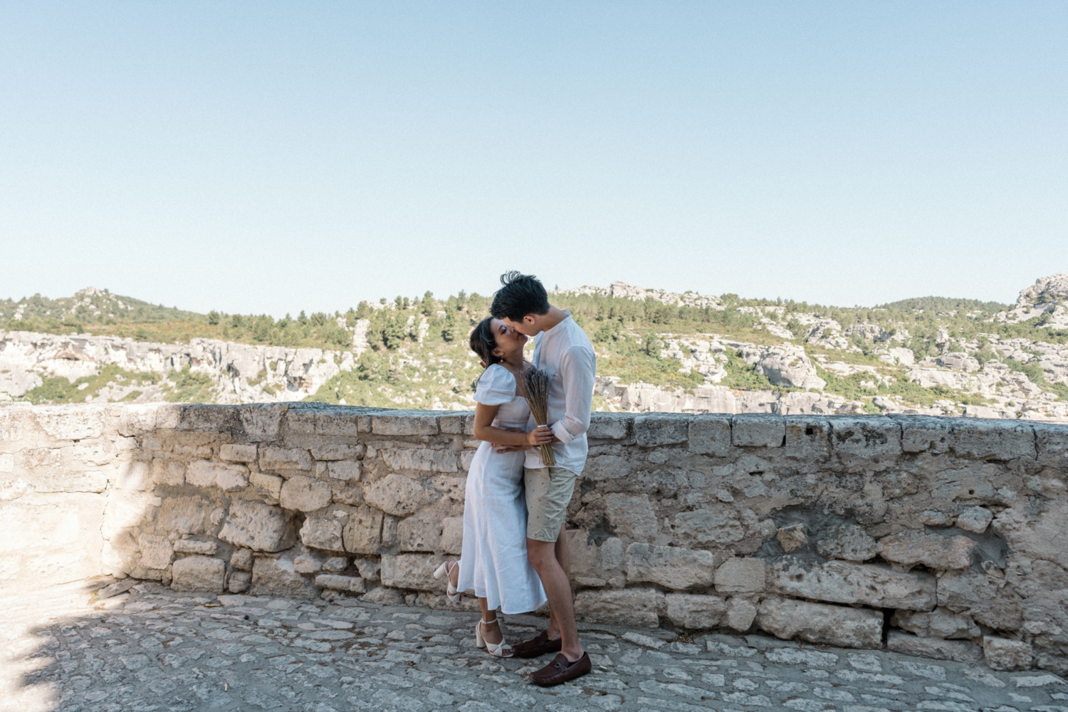 man kisses woman holding lavender bouquet in les baux de provence