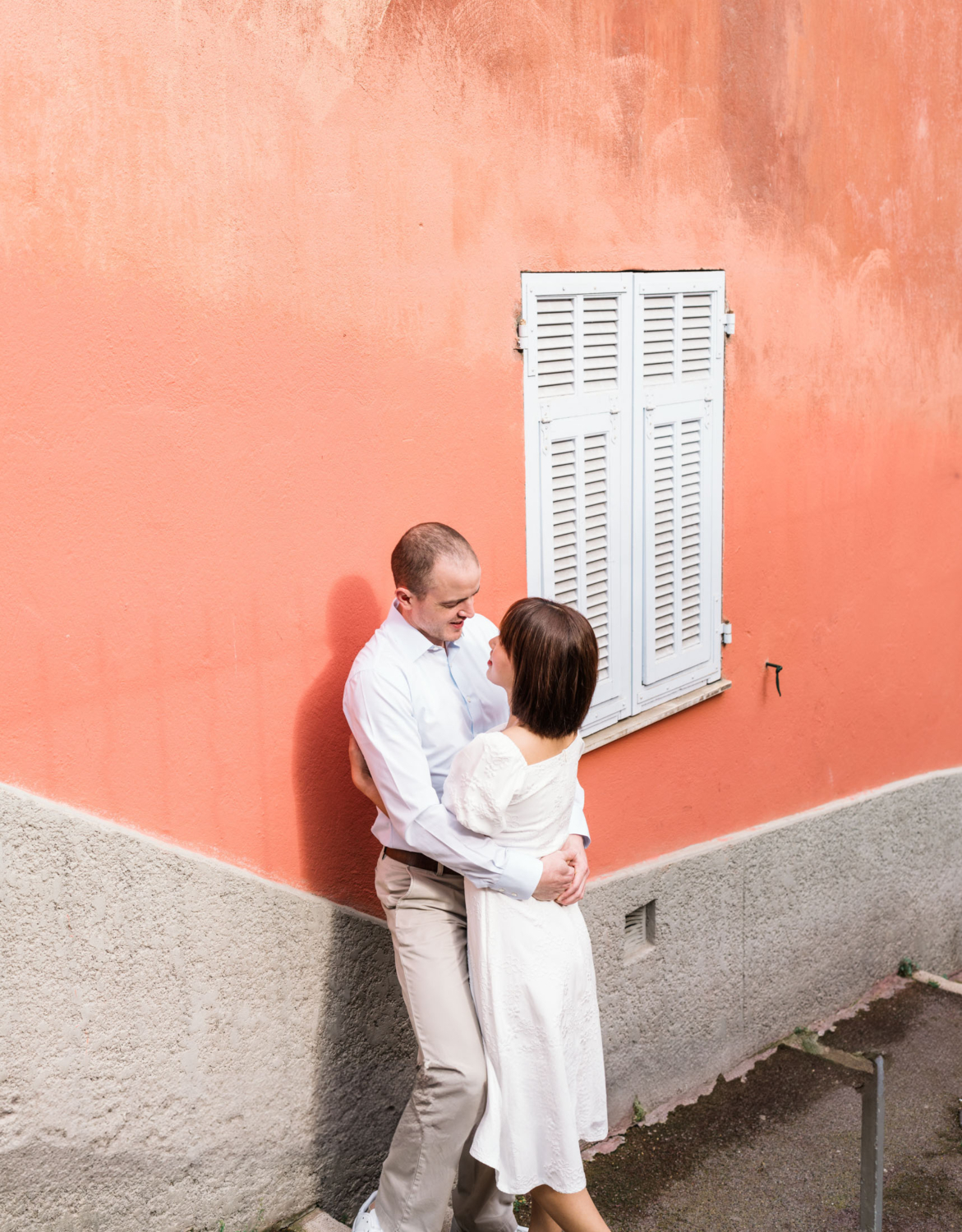 man and woman embrace next to orange colored wall in nice france