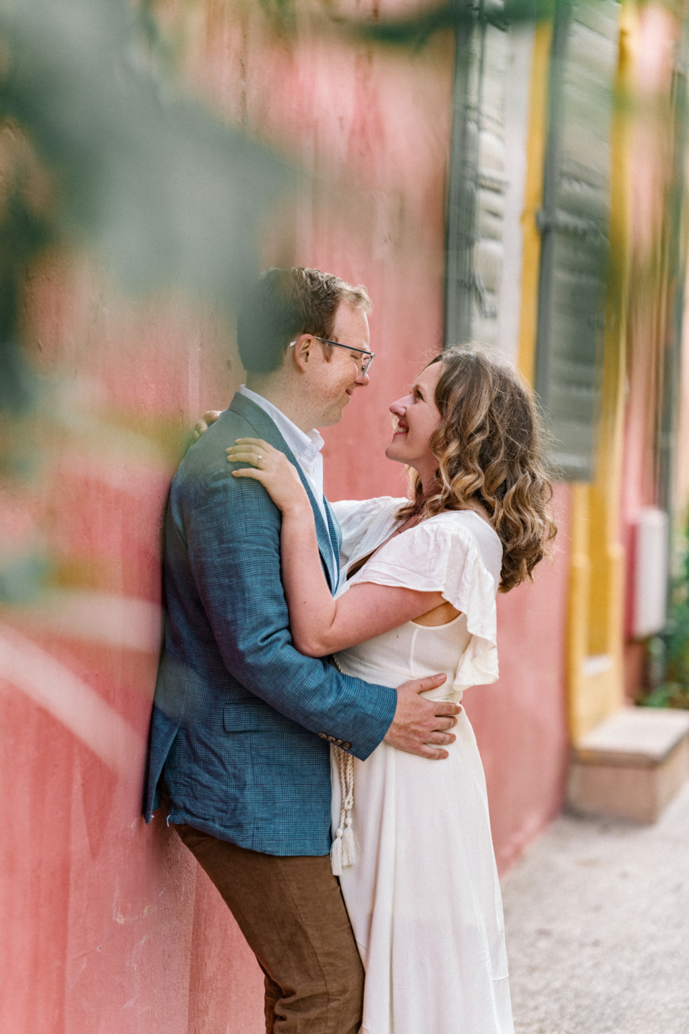 engaged couple embrace in front of colorful wall