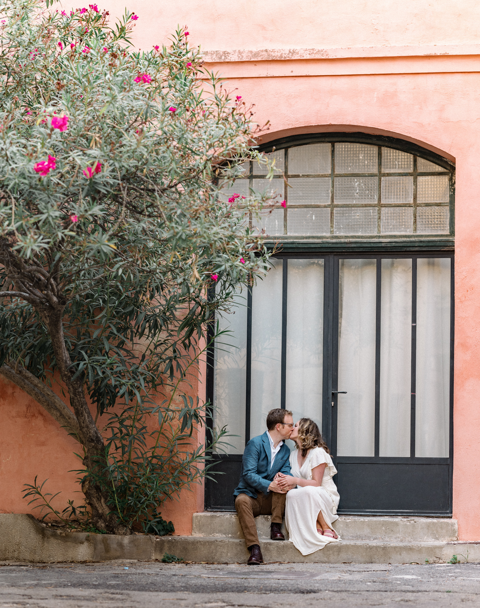 engaged couple kiss on step next to flower tree in arles france during Engagement Photos In Provence