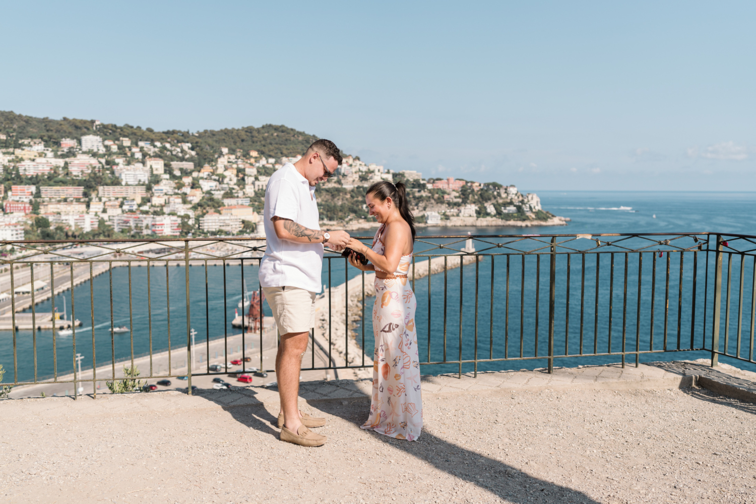 man slips diamond engagement ring on woman's finger with view of sea in nice france