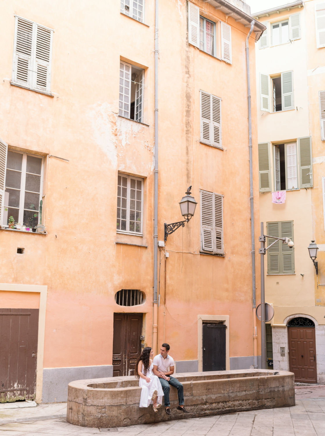 newly engaged couple sit on old lavoir in old town nice france