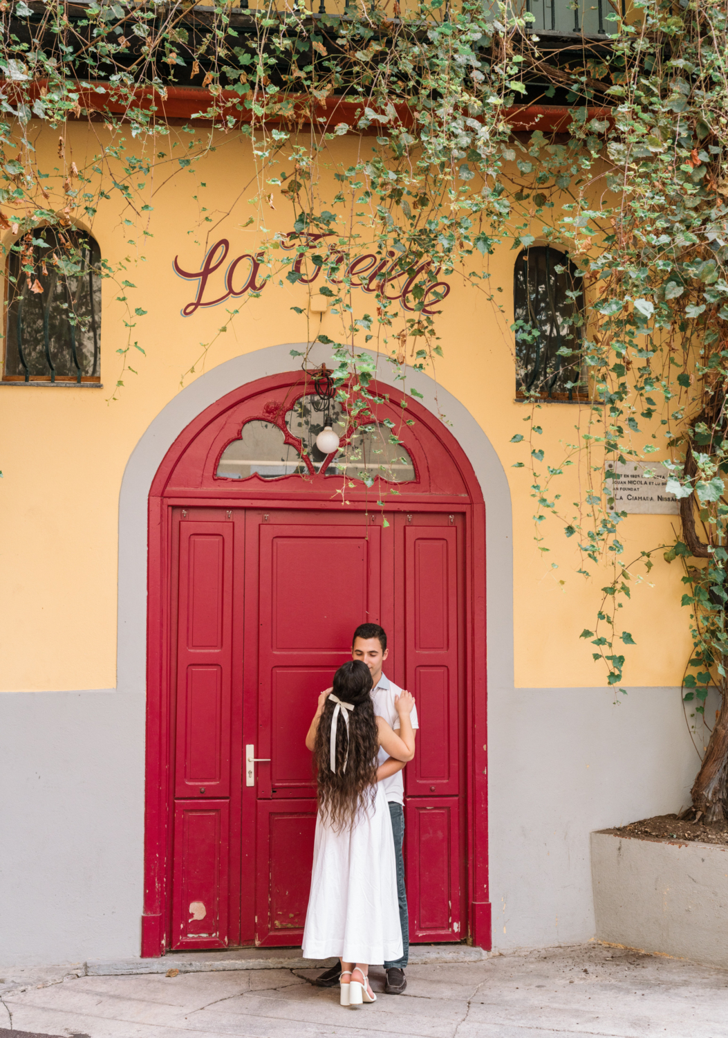 engaged couple embrace in front of red door in nice france