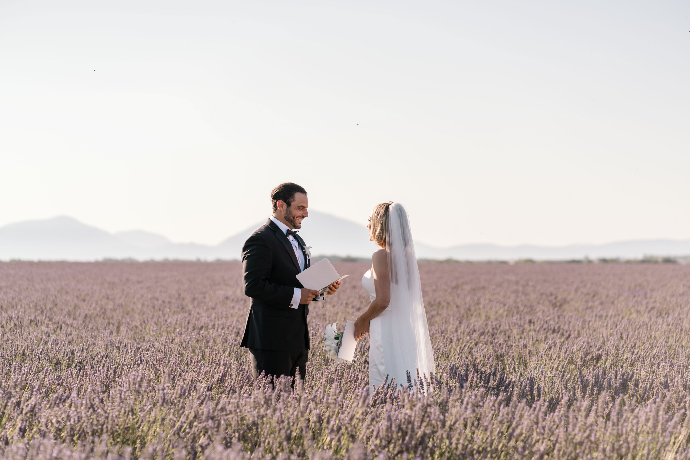 groom smiles at bride while reading vows in lavender field in provence