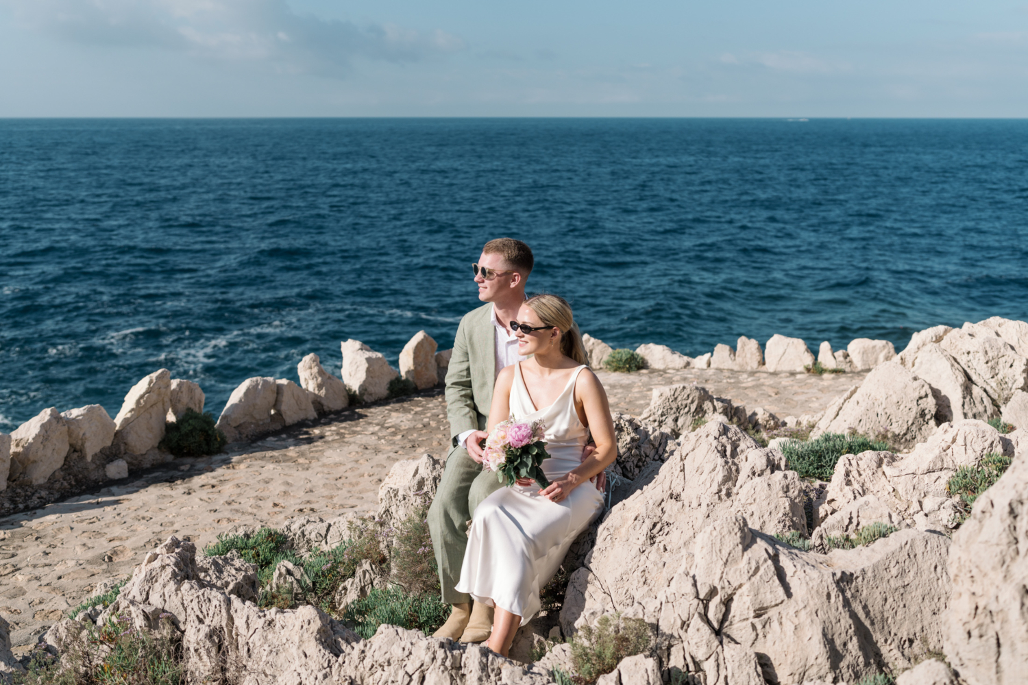 bride and groom smile and sit on rocks in saint jean cap ferrat