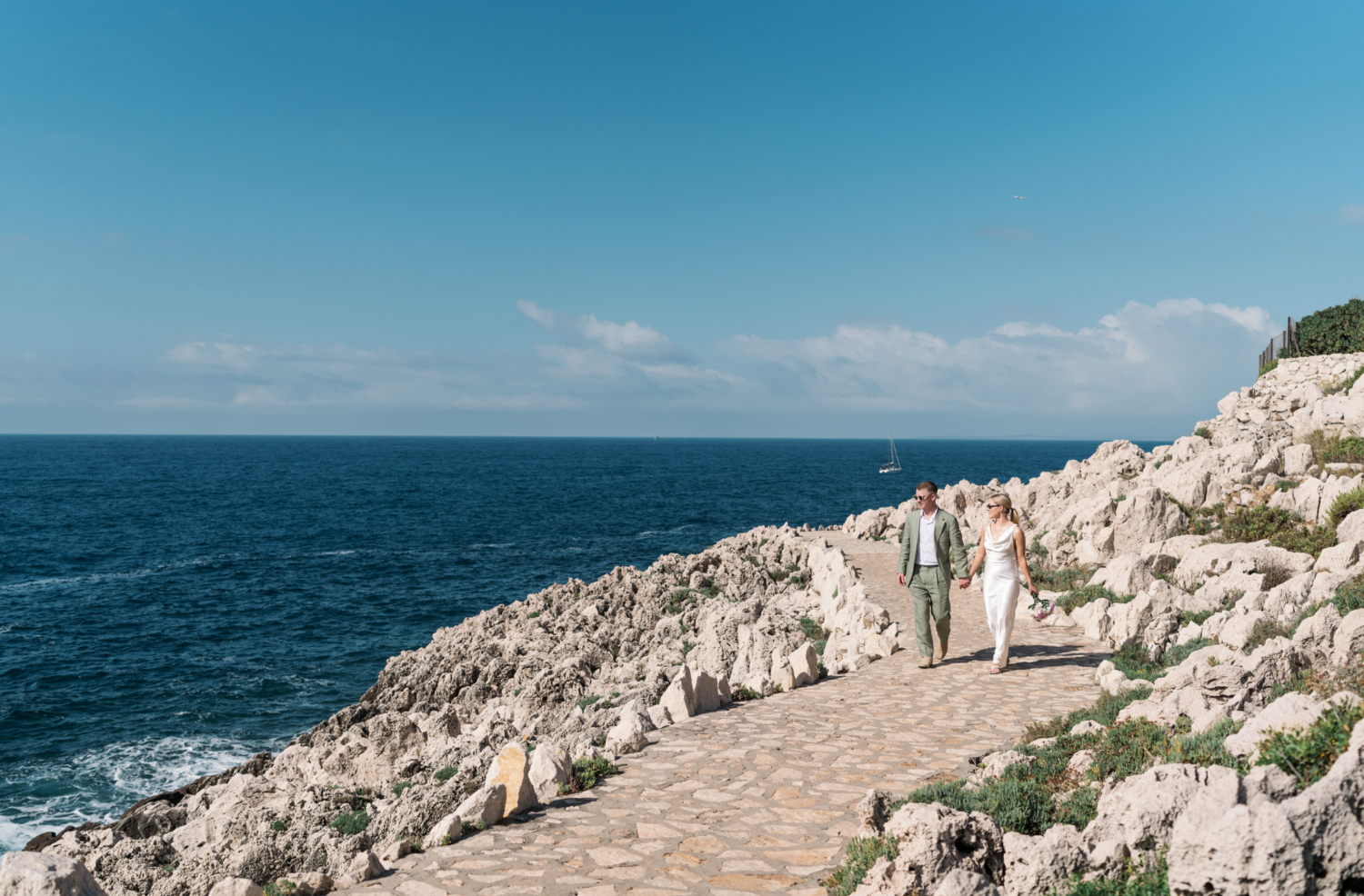 bride and groom walk holding hands with the sea in background saint jean cap ferrat