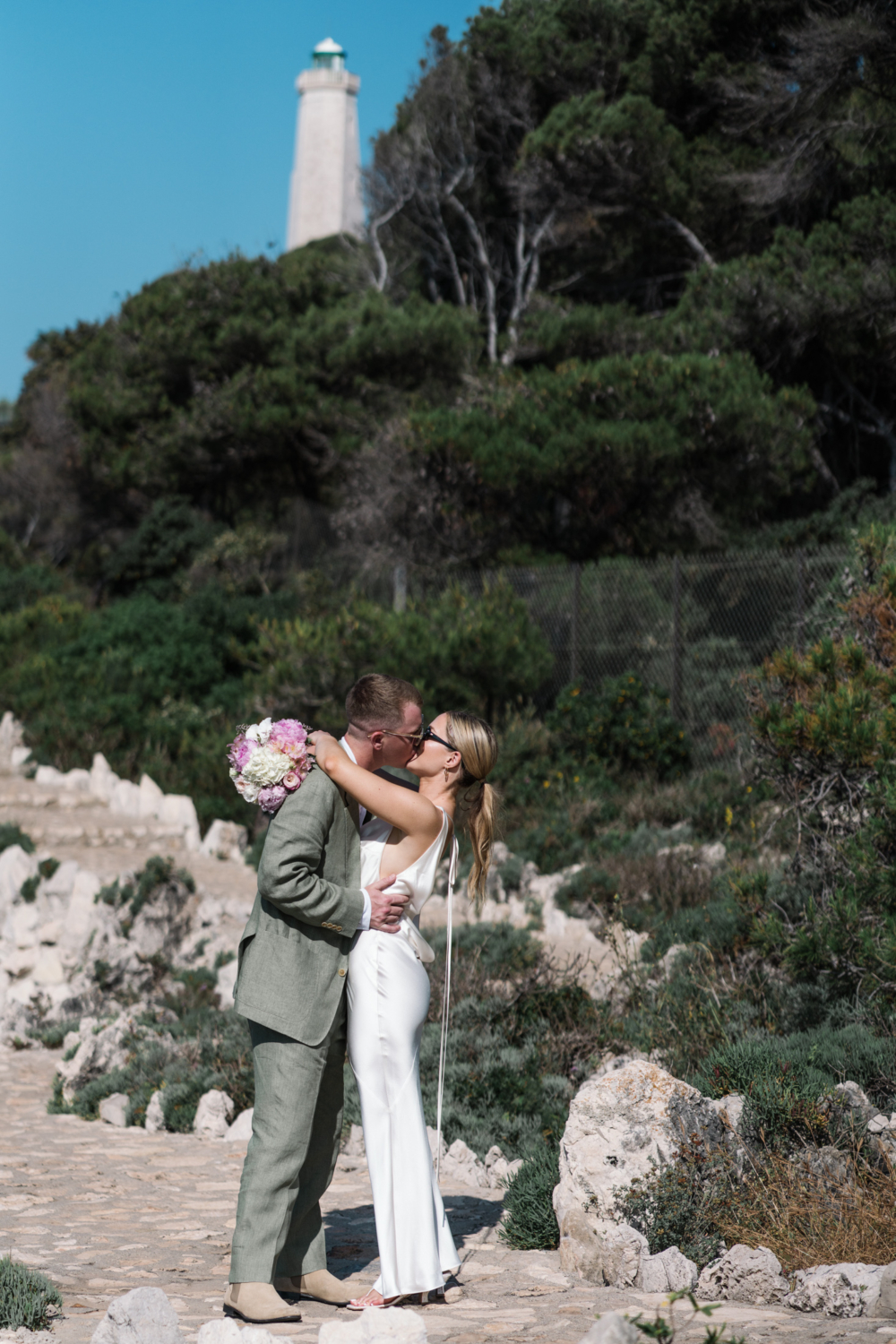 bride and groom kiss with view of lighthouse in saint jean cap ferrat