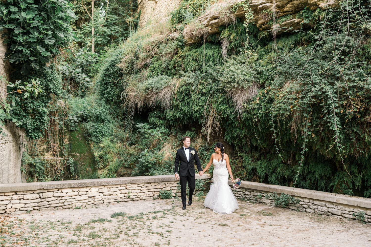 bride and groom walk by fern wall in gordes france