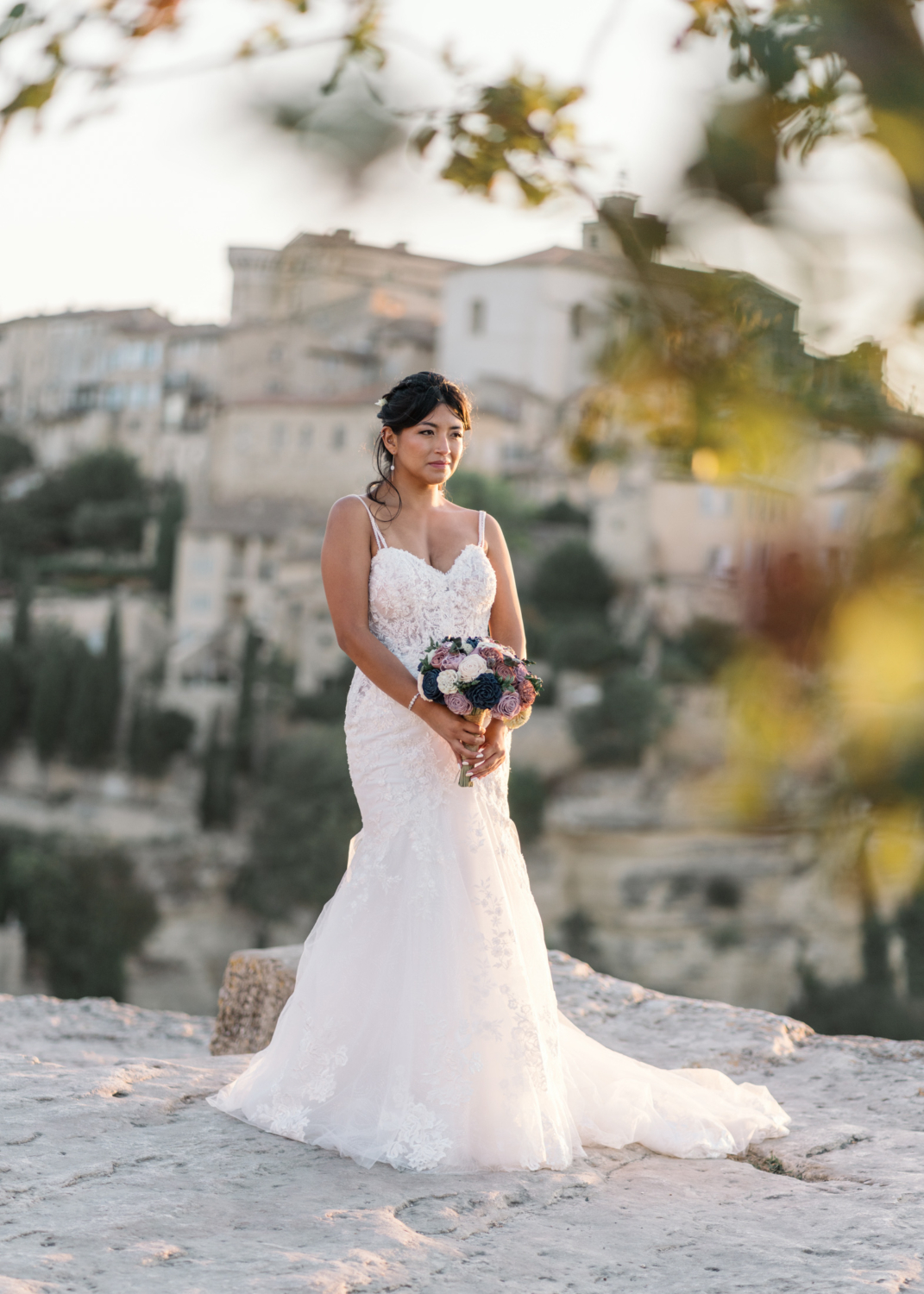 bride poses with bouquet with gordes village in background