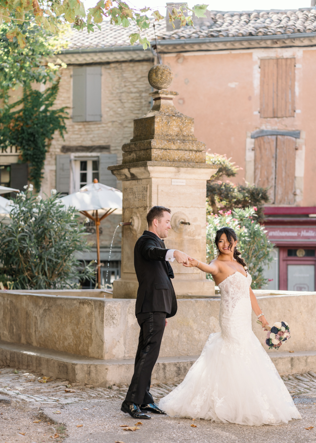 groom spins bride in dance in gordes next to fountain