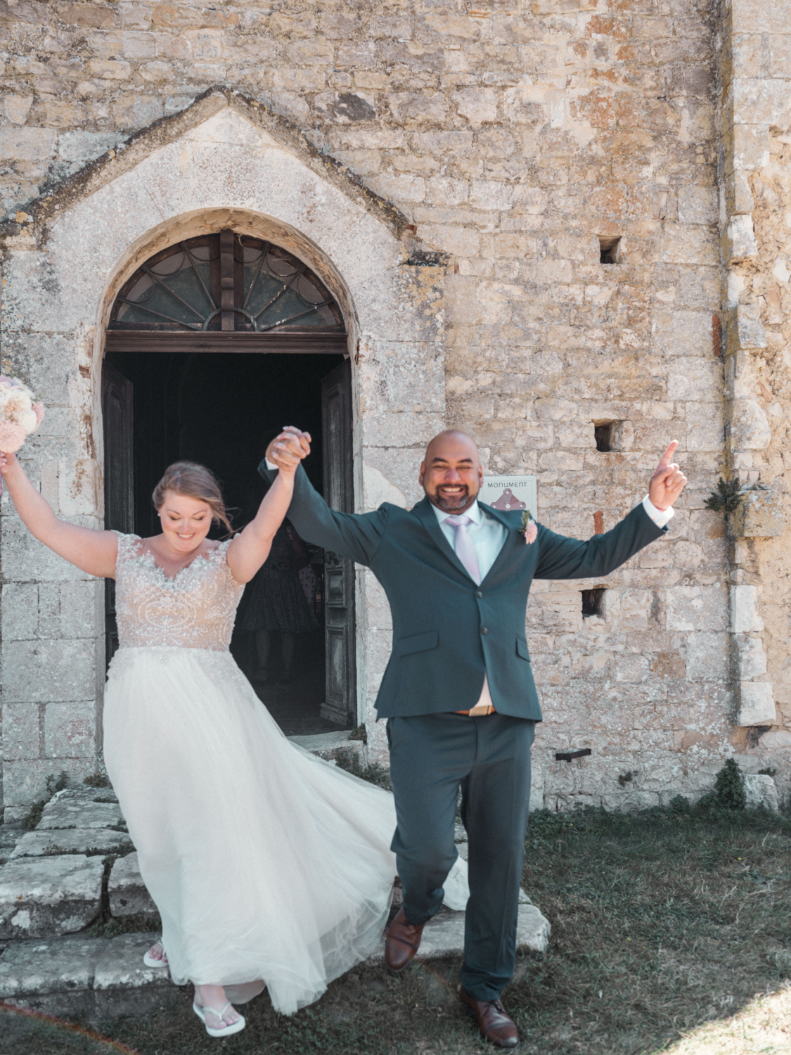 bride and groom exit church after wedding with hands in air