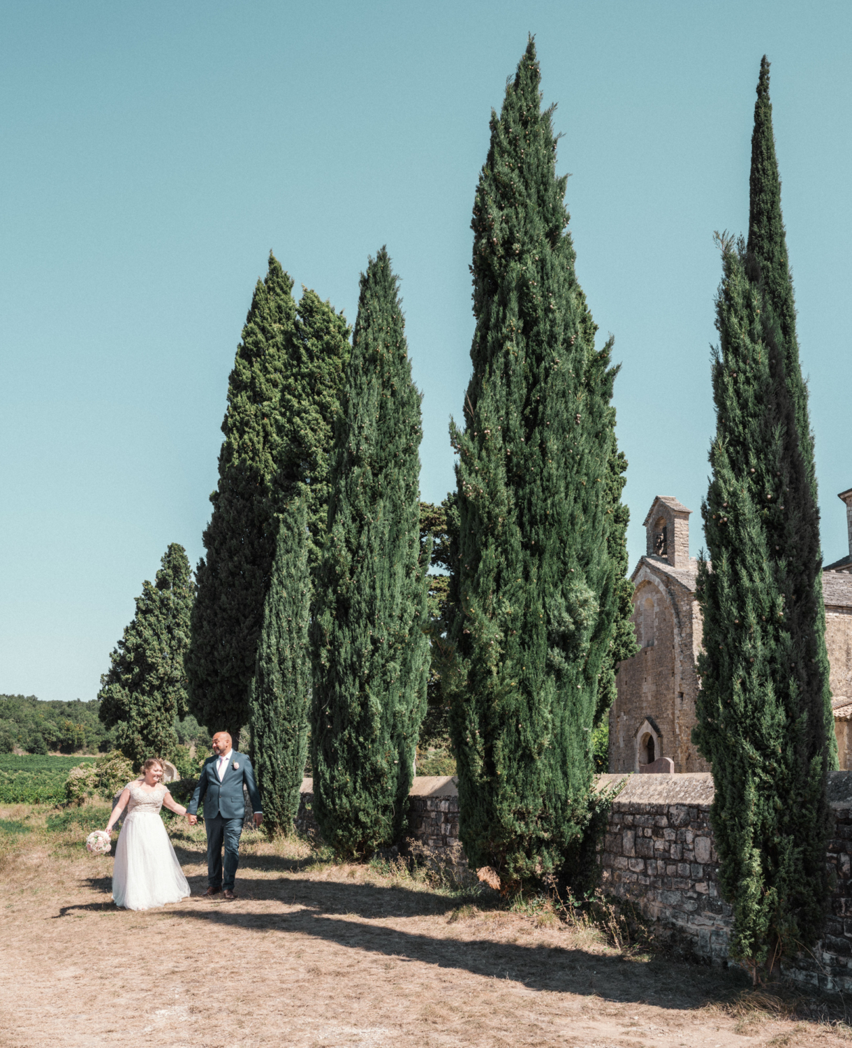 bride and groom walk hand in hand next to cyprus trees