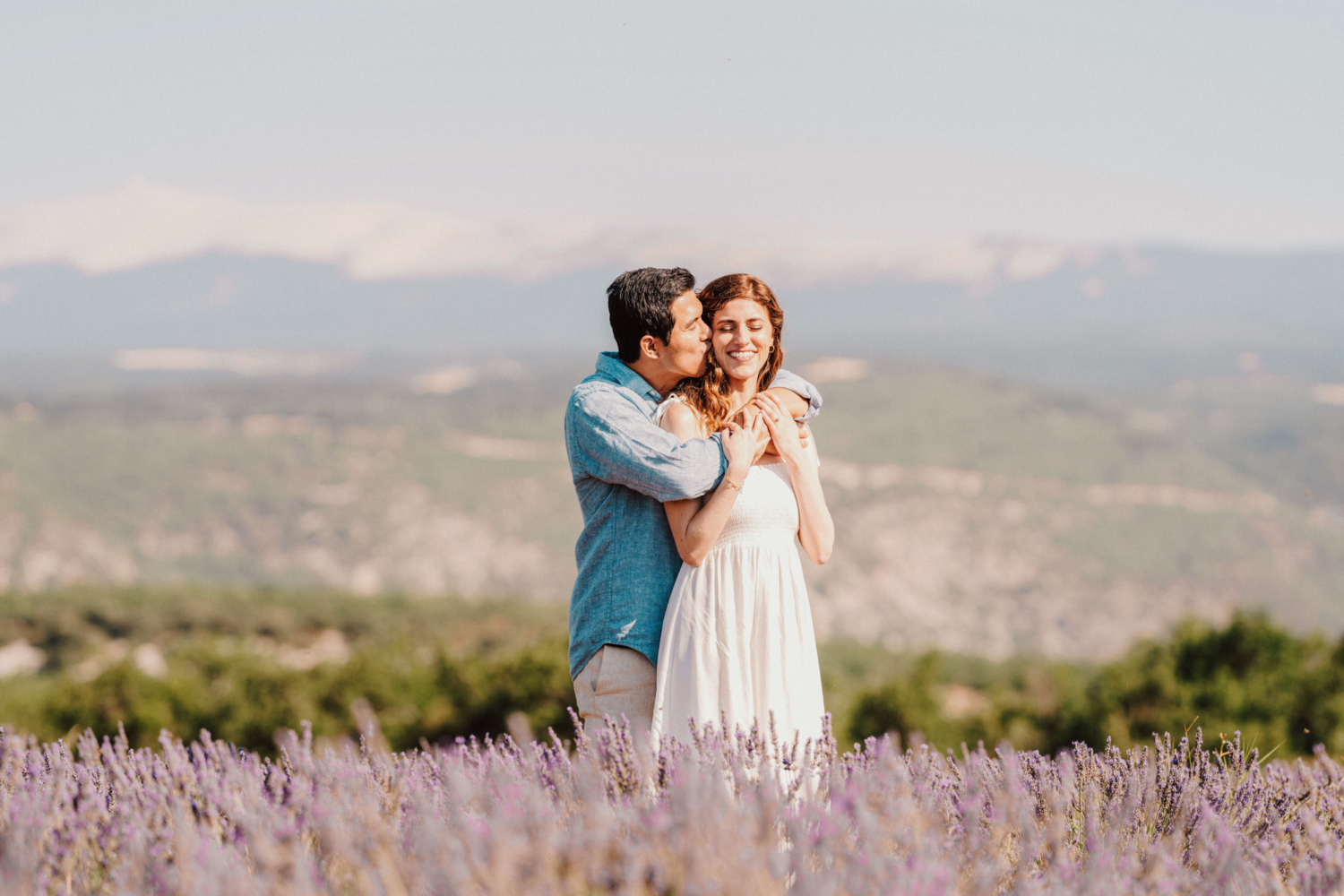 man kisses woman on side of face in lavender field