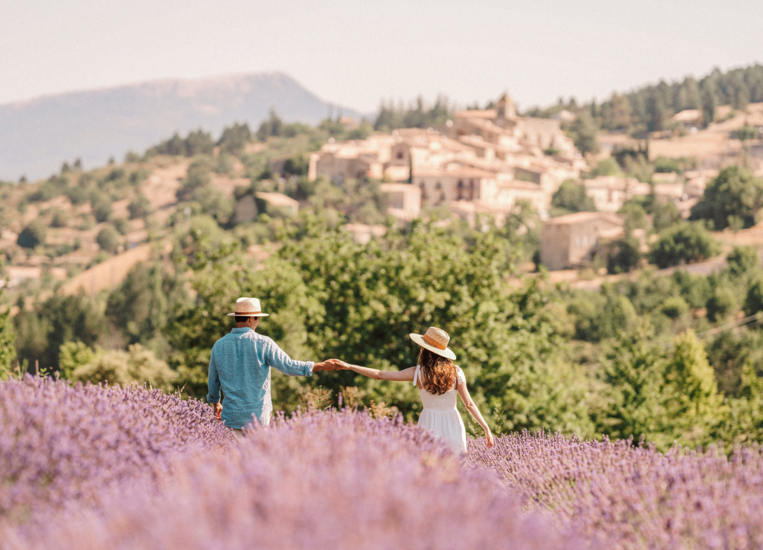 couple walk through lavender field with village in background