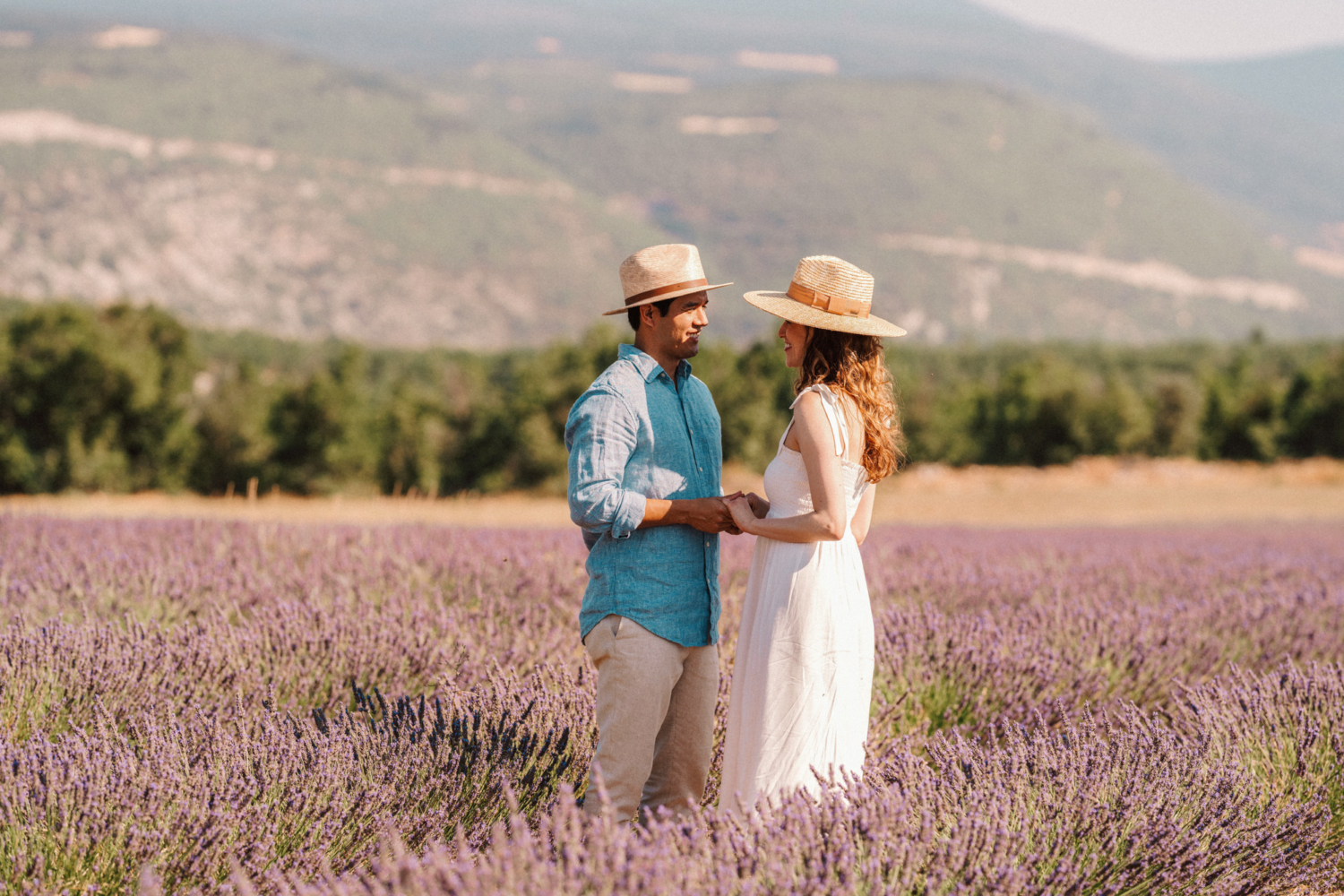 couple hold hands wearing hats in lavender field