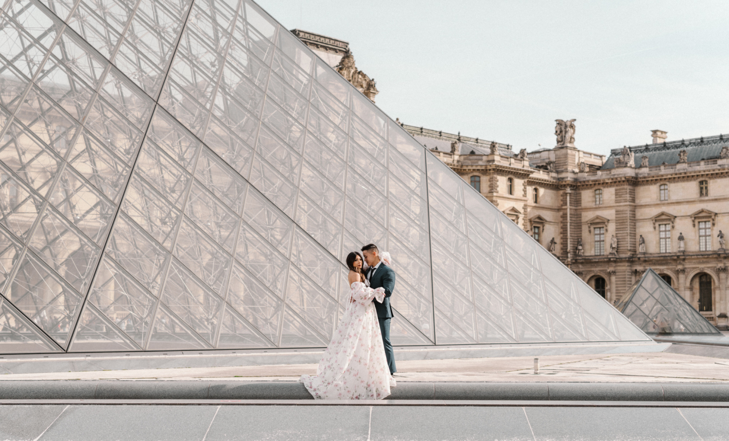 asian couple pose at glass pyramid at louvre museum paris