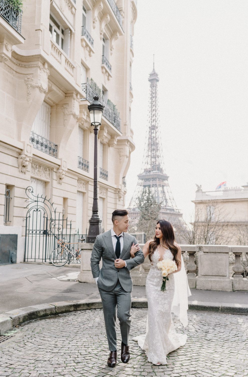asian wedding couple walking arm in arm with view of eiffel tower
