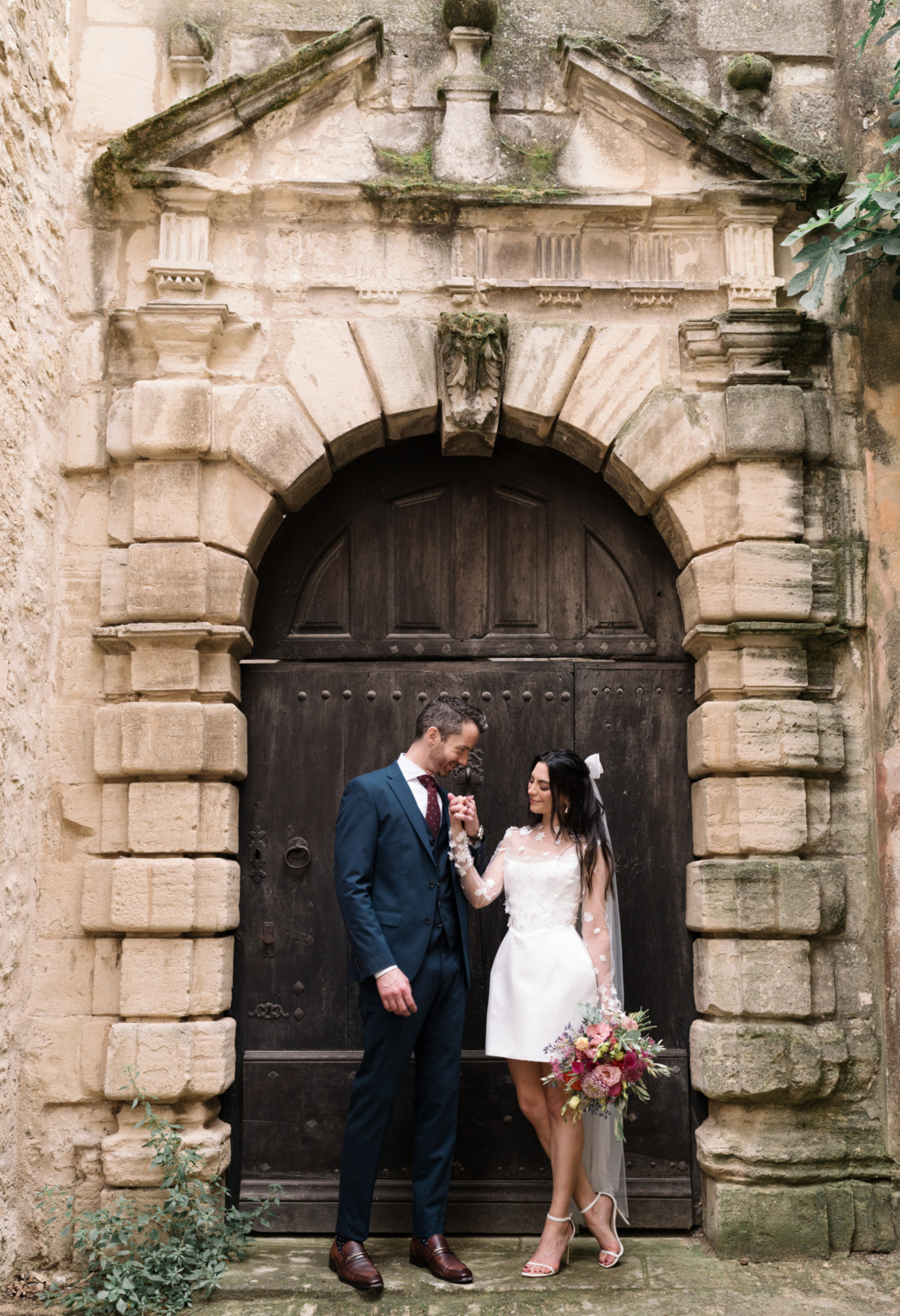 groom holds brides hand next to brown door in gordes france