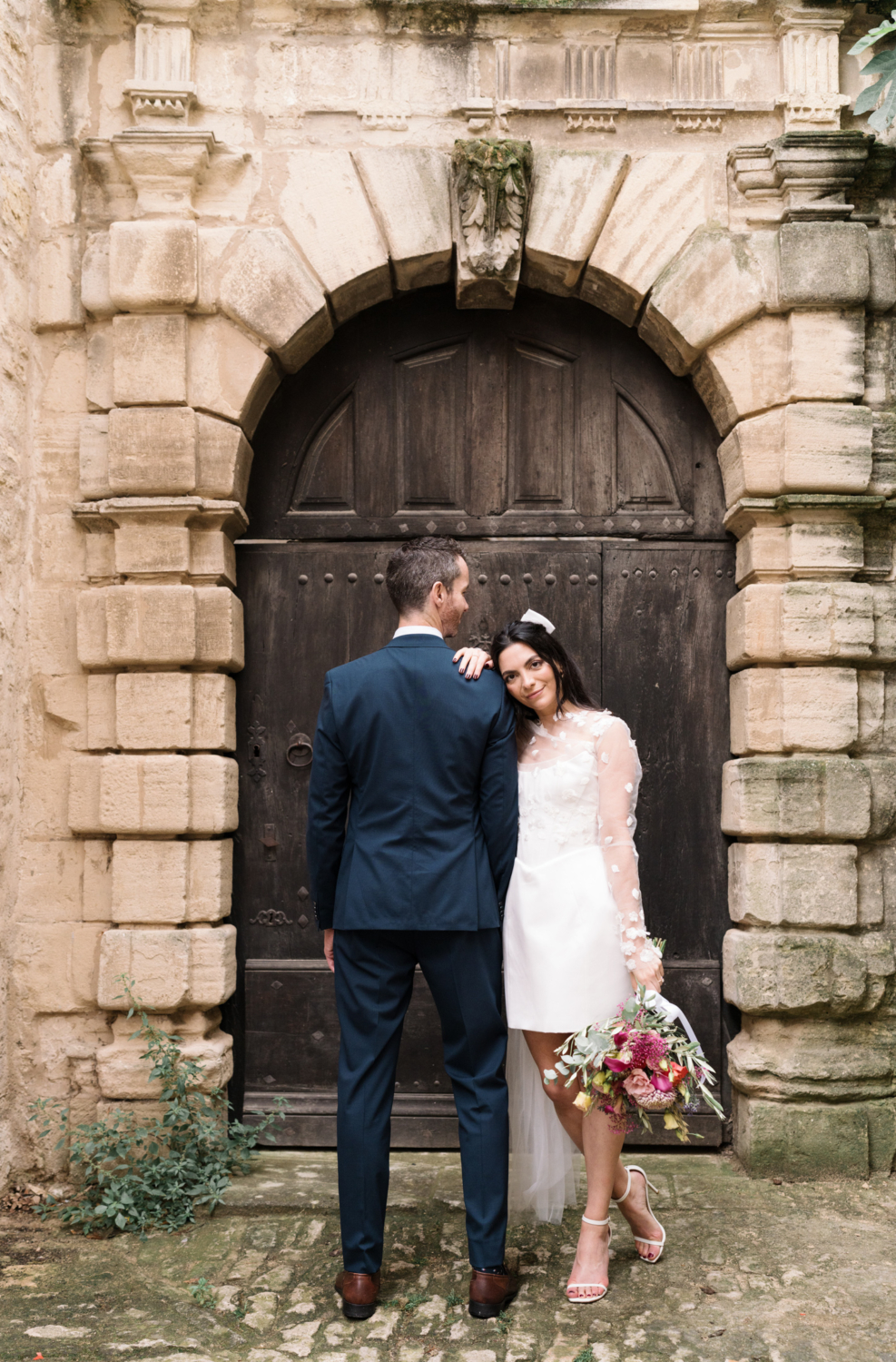 bride and groom pose standing next to a door in gordes france