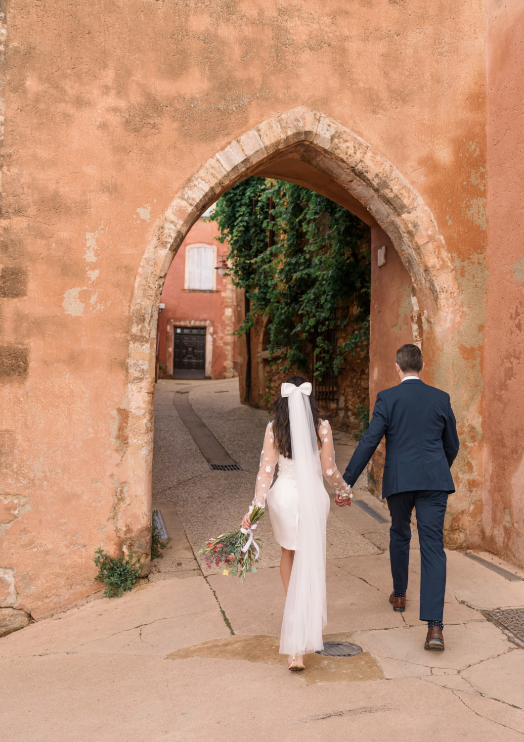 bride and groom walk hand in hand entering roussillon france