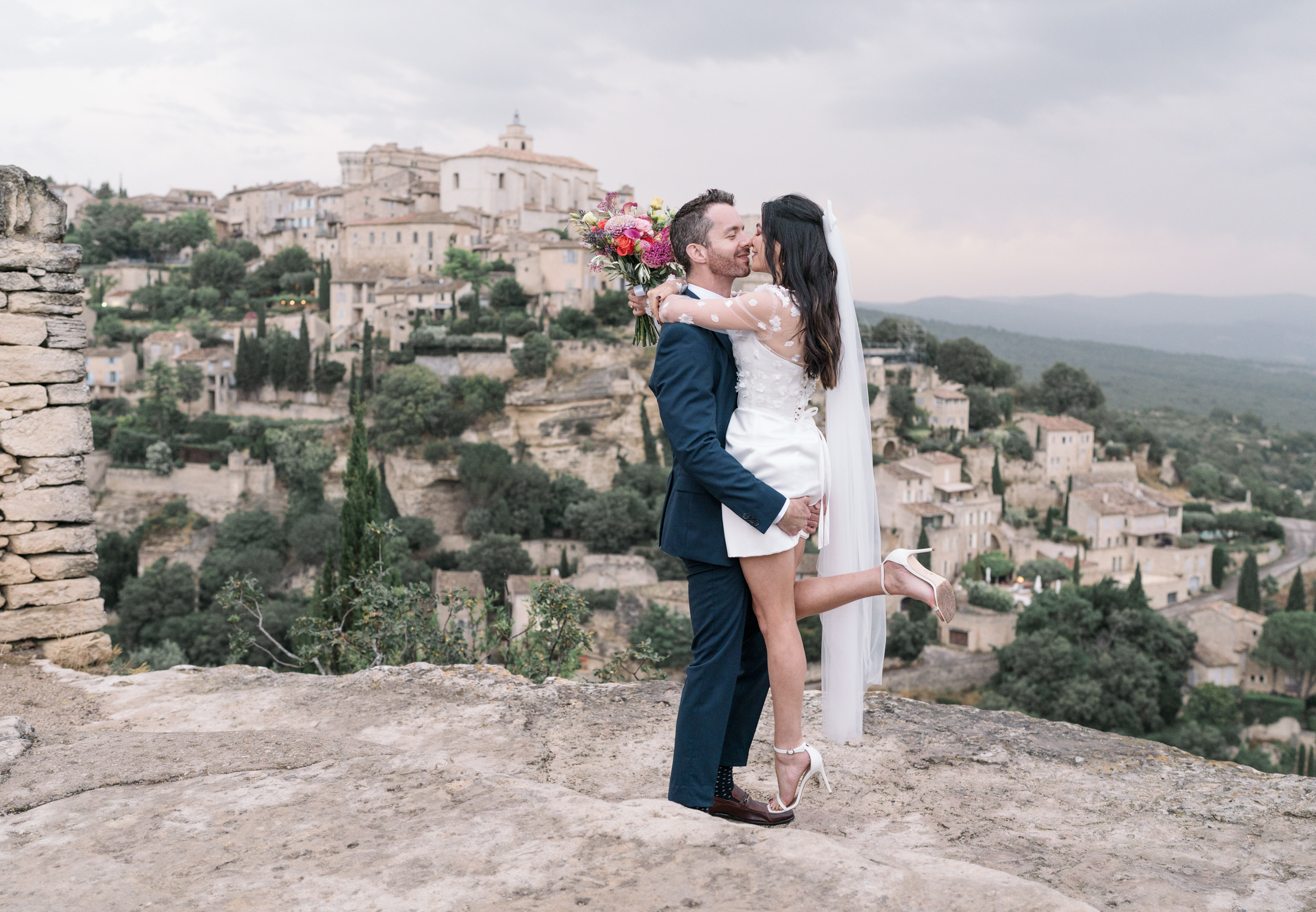 groom lifts bride in air with view of gordes france