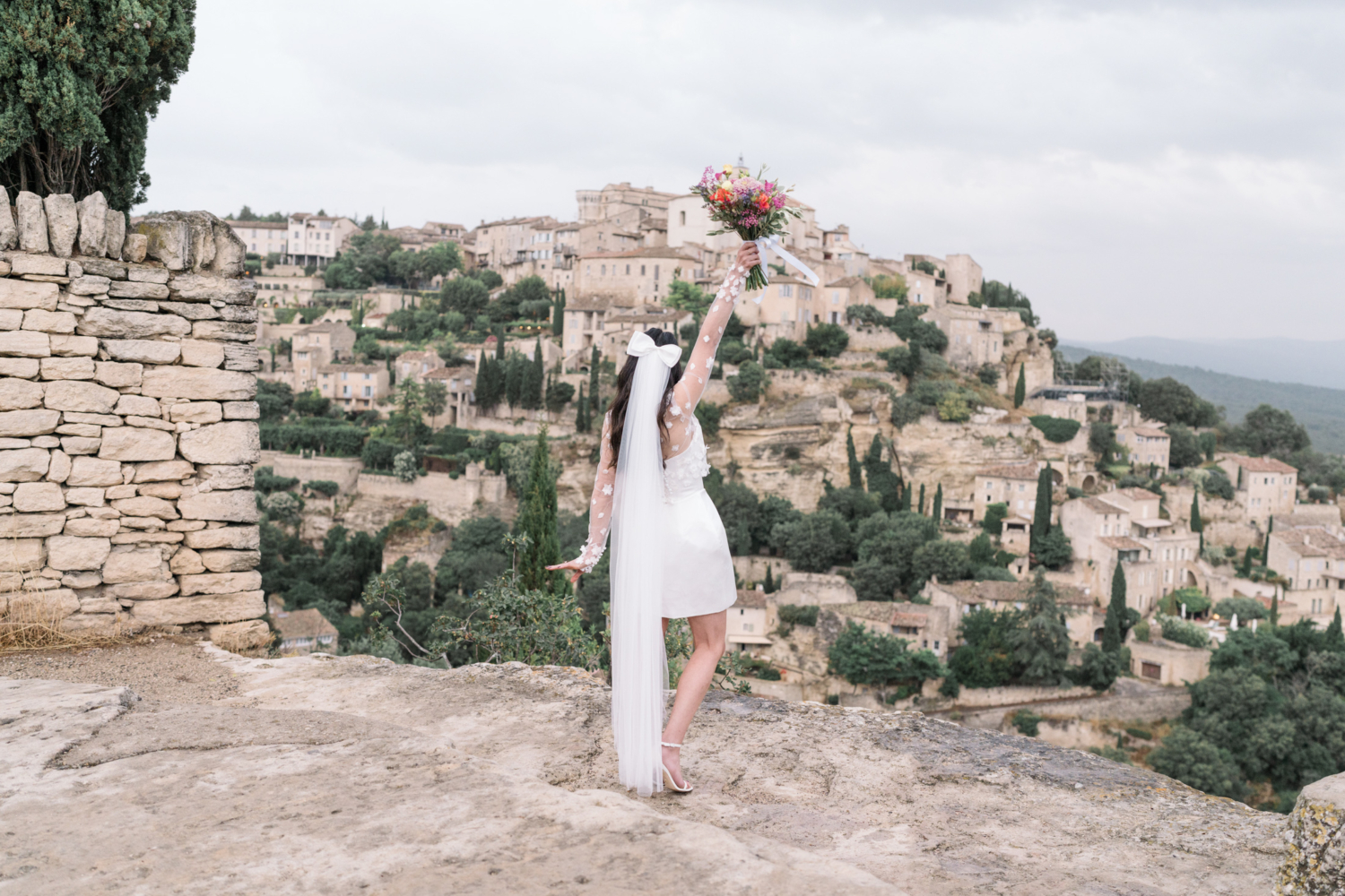 bride holds bouquet in air in gordes france