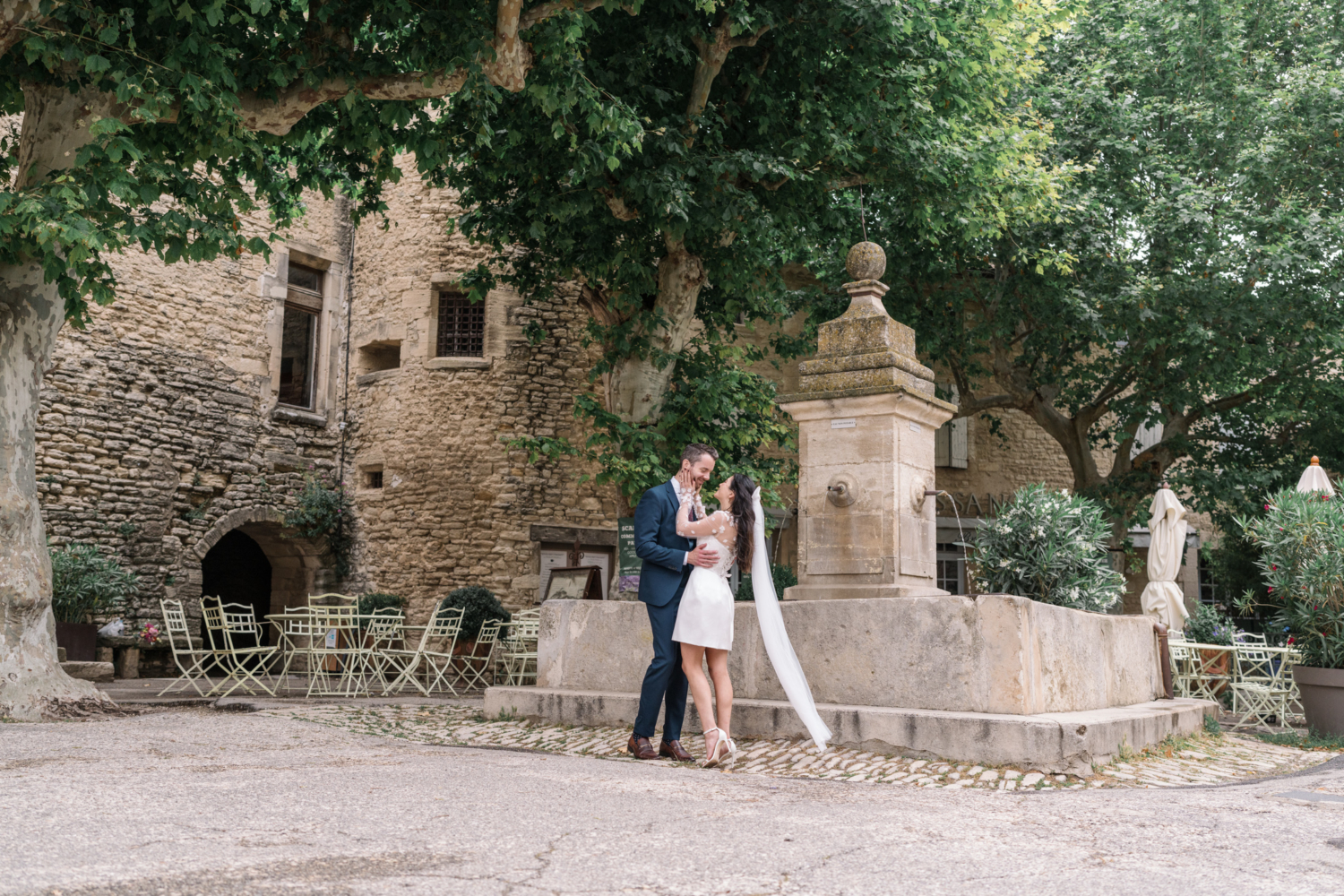 bride and groom embrace and laugh next to fountain in gordes france