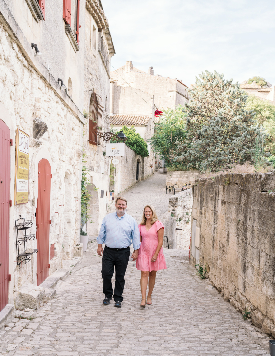 husband and wife walk hand in hand smiling in les baux de provence france