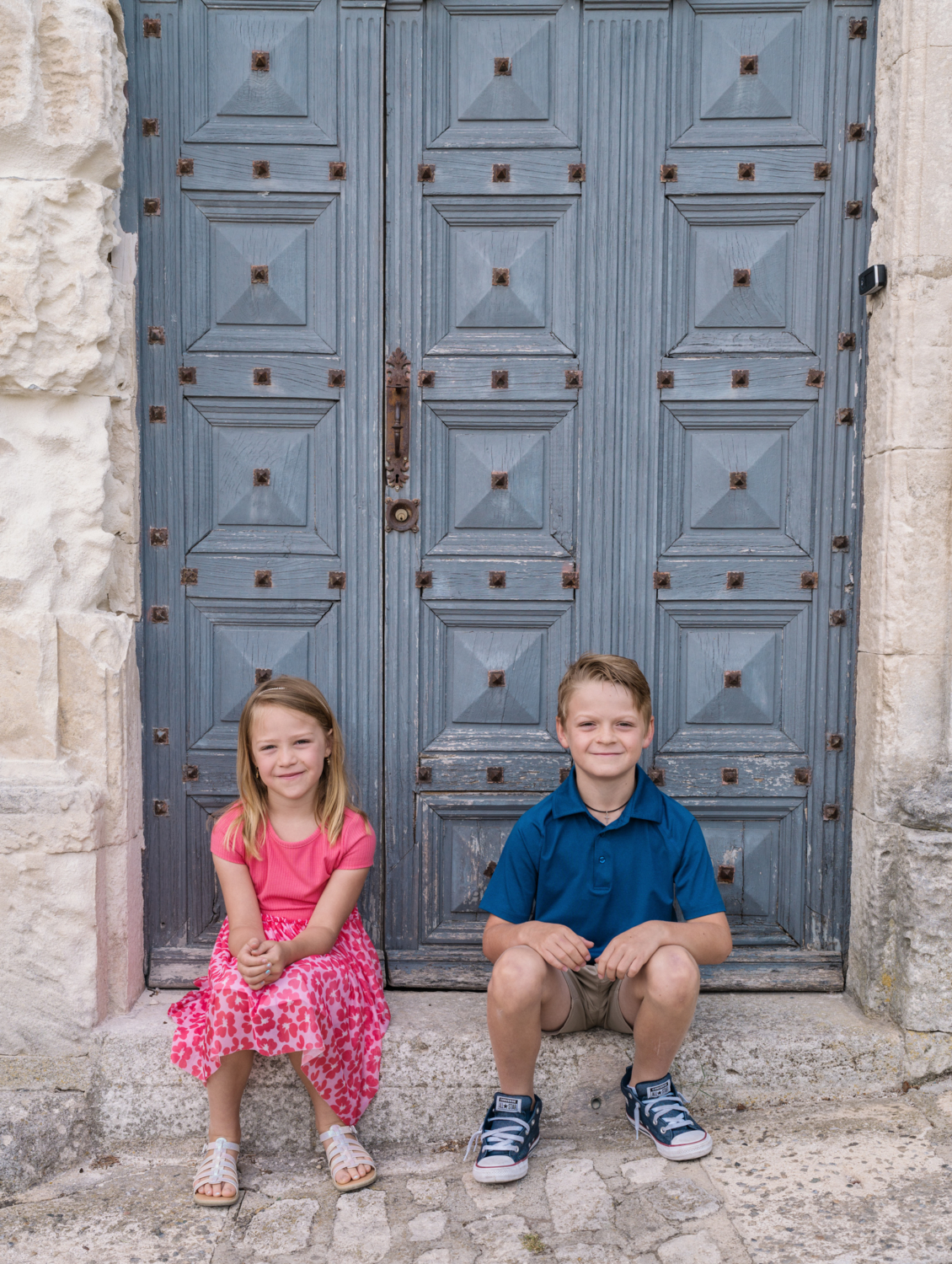 kids sit in front of historic blue door in les baux de provence france