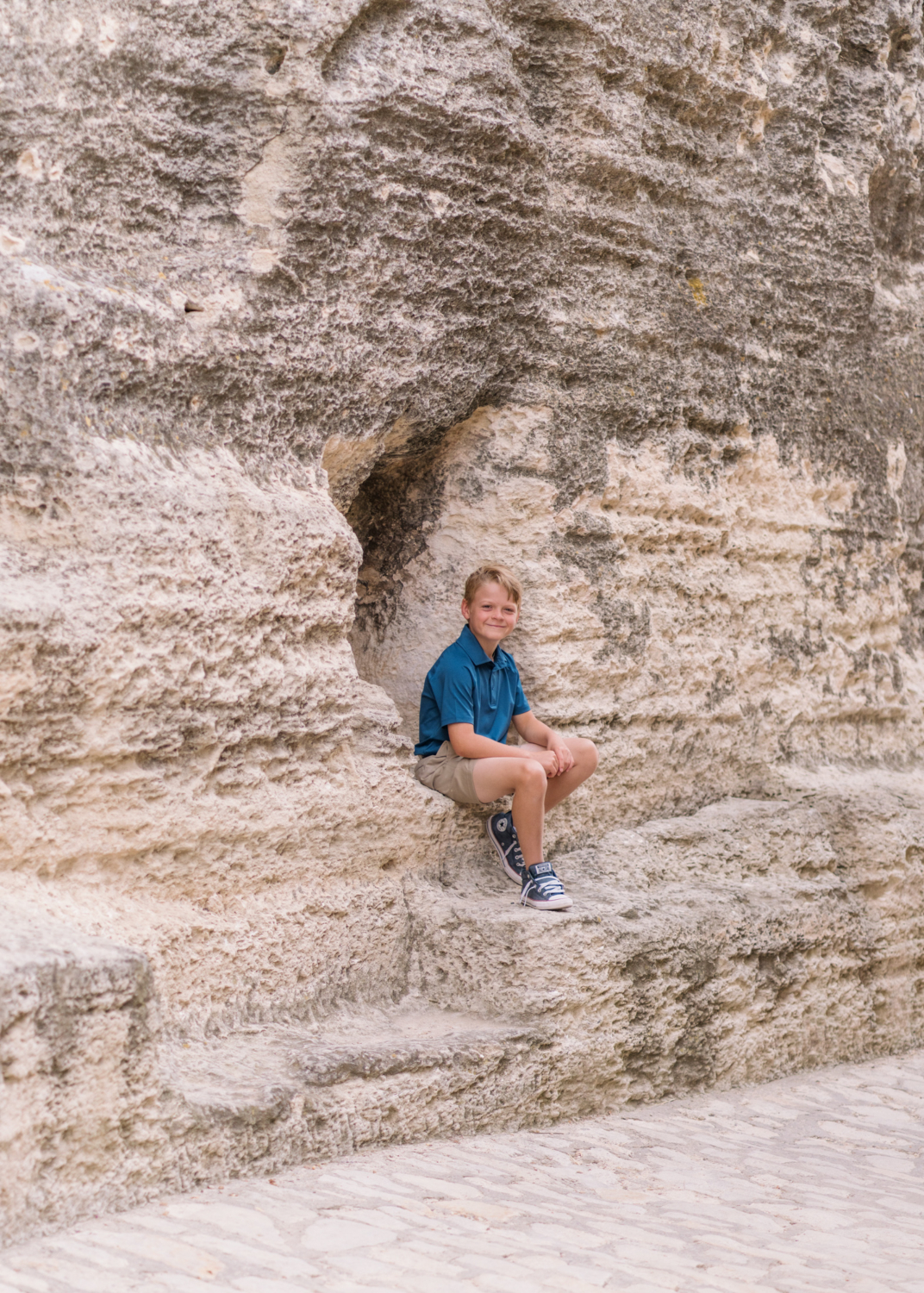 young boy sits in a cave in les baux de provence